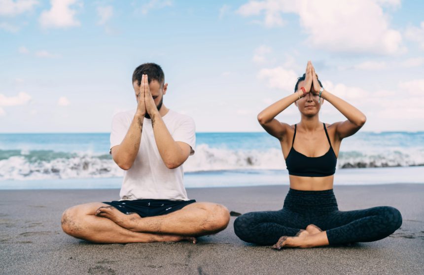 Athletic friends breathing and feeling harmony mindfulness in asana near ocean