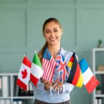 Happy female tutor showing bunch of diverse flags, recommending foreign language studying school