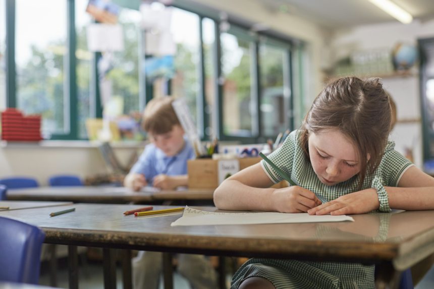 Schoolgirl writing in classroom lesson in primary school