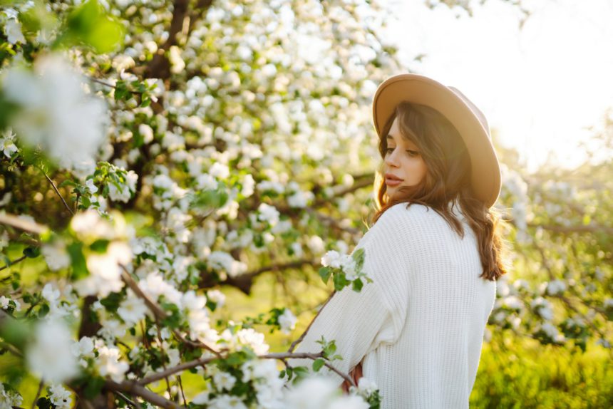 Smiling woman with hat posing in blooming spring park. The concept of relax, travel. Fashion style.