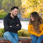 Young people on a first date sitting on a wooden bench in a park and laughing