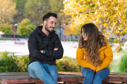 Young people on a first date sitting on a wooden bench in a park and laughing